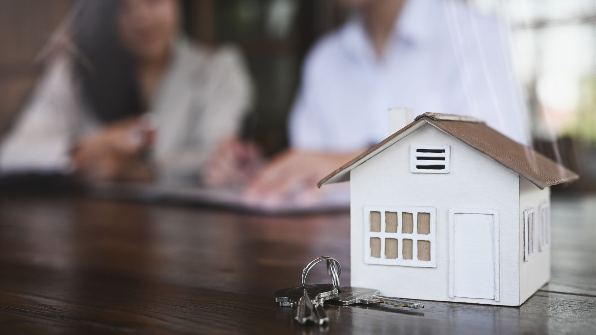 Close up view small house model and house keys on wooden table. New house, insurance and real estate concept.